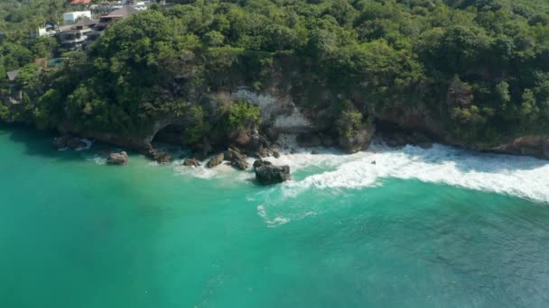 Dzikie fale oceaniczne rozbijają się na skalistym klifie na tropikalnym wybrzeżu Bali. Widok z lotu ptaka turkusowo-niebieskiej wody wokół skalistych klifów — Wideo stockowe