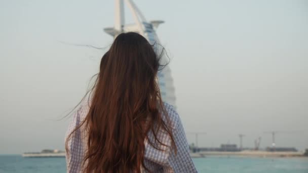 Woman looking at Burj Al Arab hotel in Dubai during sunset. Back view of female tourist looking at famous tourist attraction in Dubai — Stock Video