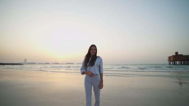 Ritratto di donna attraente sulla spiaggia con paesaggio urbano di Dubai sullo sfondo. Donna con lunghi capelli castani e abiti eleganti in piedi sulla spiaggia di Dubai — Video Stock