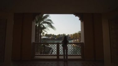 Dubai 'deki lüks oteldeki su kanalına bakan bir kadın. Dolly, nehir kıyısındaki oteldeki köprüde palmiye ağaçları ve restoranlarla çevrili bir kadın turist olarak görülüyor.