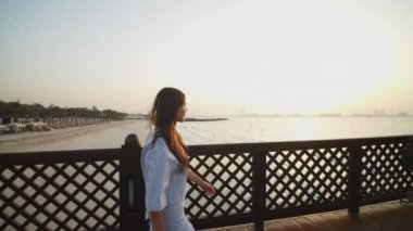 Gün batımında iskelede yürüyen bir kadın. Arka planda Dubai silueti olan, ahşap iskelede yürüyen bir kadının yan görüntüsü