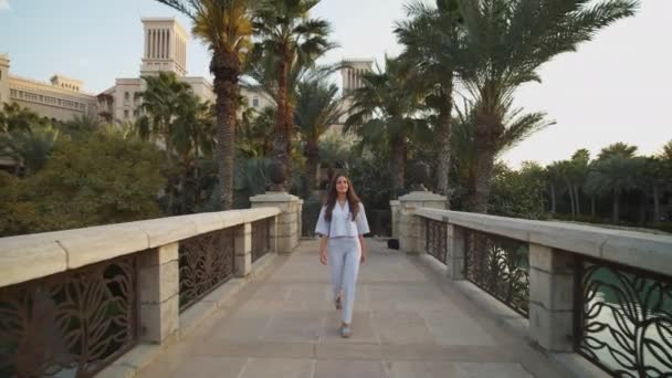 Женщина, идущая по мосту с роскошными жилыми зданиями на заднем плане. Вид спереди женщины, гуляющей в роскошных кварталах Дубая — стоковое видео