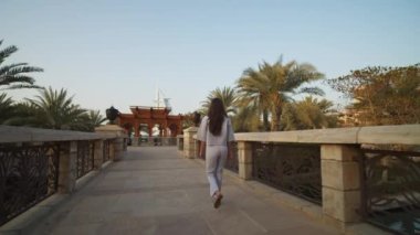 Arka planda Burj Al Arab 'la Dubai' de köprüden geçen bir kadını takip etmek. Birleşik Arap Emirlikleri 'nde lüks mahallede yürüyen çekici bir kadın.