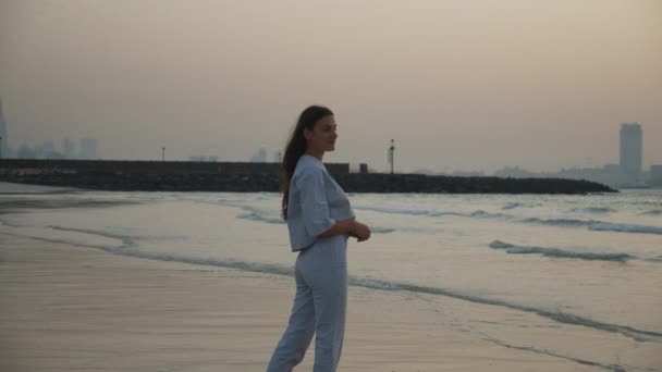 Mujer morena en ropa elegante de pie en la playa de arena durante el atardecer en Dubai — Vídeo de stock