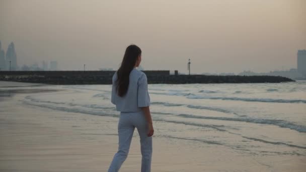 Giovane donna che cammina tra le onde sulla spiaggia di sabbia durante il tramonto a Dubai — Video Stock