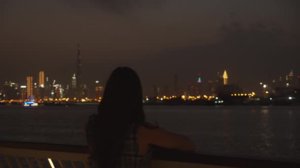Kvinnan tittar på Dubai skyskrapor på natten. Dubai skyline med ljus i staden — Stockvideo