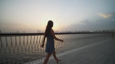 Arka planda Dubai silueti olan deniz kenarında yürüyen bir kadın. Dubai 'de akşam yürüyüşünün tadını çıkaran bir turist.