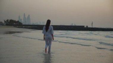 Dubai 'de gün batımında okyanus kıyısında yürüyen esmer bir kadın.