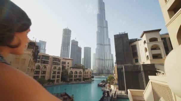 Toeristen kijken uit op het stedelijk centrum van Dubai met Burj Khalifa wolkenkrabber. Dolly uit het zicht van een vrouw op een balkon met uitzicht op luxe toeristische resort bij het zwembad — Stockvideo