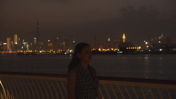 Femme marchant sur la jetée près des toits de Dubaï la nuit. Belle femme brune profitant d'une promenade nocturne avec des gratte-ciel de Dubaï en arrière-plan — Video