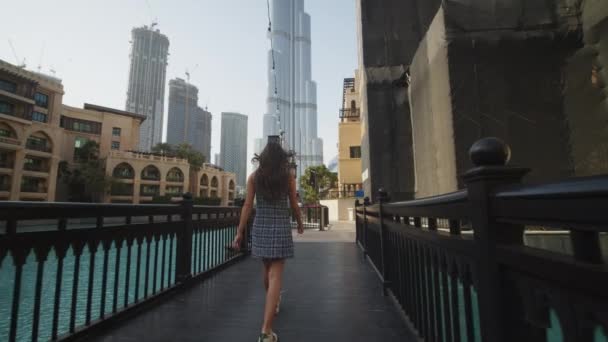 Femme marchant dans une station touristique de luxe près du gratte-ciel Burj Khalifa à Dubaï. Promenade touristique autour du complexe d'appartements de luxe et des restaurants près de la piscine à Dubaï — Video