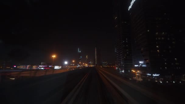 Le métro de Dubaï passe devant les gratte-ciel du centre-ville la nuit. Vue à la première personne d'un train de métro circulant rapidement sur une voie de métro — Video