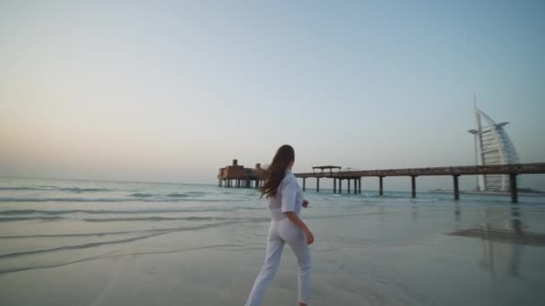 Young woman running barefoot on the beach in Dubai with with Burj Al Arab in the background — Stock Video