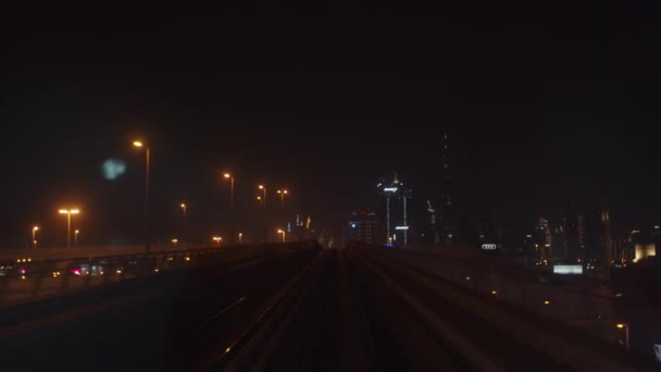 Dubai tunnelbanetåg kör uppför på utomhusbanan. Tunnelbanetåg kör på spår på natten med skyskrapor i Dubais centrum i bakgrunden — Stockvideo