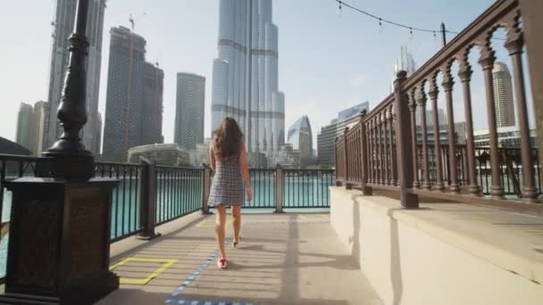 Mulher caminhando na piscina perto do arranha-céu Burj Khalifa em Dubai. Seguindo um turista explorando destinos turísticos famosos em Dubai — Vídeo de Stock