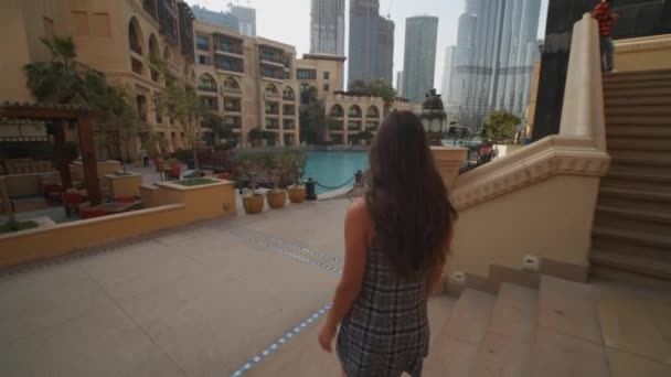 Suivre une femme marchant dans le centre-ville urbain de Dubaï avec Burj Khalifa gratte-ciel. Promenade touristique dans un hôtel de luxe avec piscine à Dubaï — Video