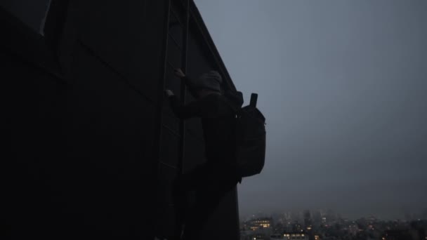 夜にニューヨークの超高層ビルの屋根の上にバックパッククライミングの男。ニューヨークの超高層ビルの側のはしごを登る男 — ストック動画