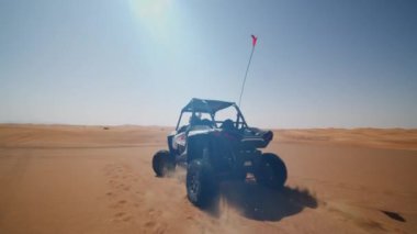 Çölde kum arabası sürüyor. Arkasında toz bulutuyla çöldeki kum tepelerine doğru giden hızlı bir off road aracı.