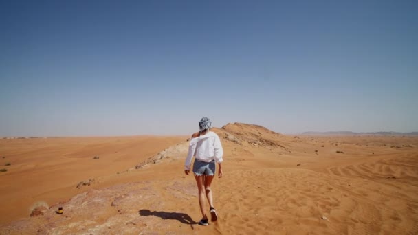 Za mladou ženou kráčející po písečných dunách. Mladá žena s zakrytou hlavou kráčející v poušti poblíž Dubaje — Stock video