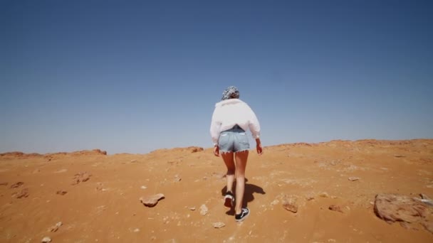 Mujer joven caminando por la duna de arena a la vista panorámica del desierto. Turista en camisa y jeans explorando el desierto cerca de Dubai — Vídeo de stock