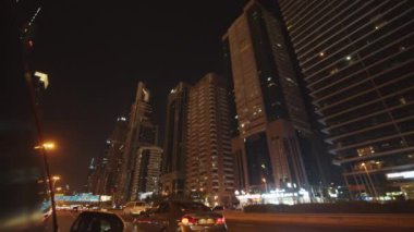 Gece Dubai 'de çok şeritli otoyolda araba kullanmak. Ana yolda giden arabalar şehir merkezinde yüksek gökdelenlerle çevrili.