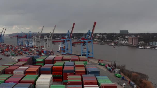 Vista aérea baja de grúas de carga y contenedores de colores junto al río en el puerto de Hamburgo — Vídeo de stock