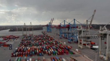 Hamburg sanayi limanındaki renkli konteynırların üstündeki büyük yük vinçlerinin görüntüsünde yavaş hava kulesi