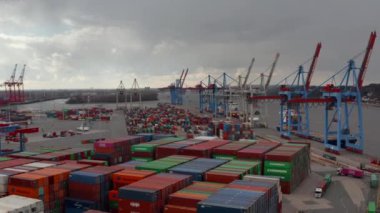 Hamburg 'daki uluslararası nakliye limanında renkli kargo konteynırları ve endüstriyel makineler üzerinde yavaş hava kulesi