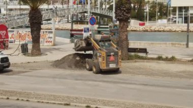 Küçük tekerlekli ön yükleyici temizlik için bir cihaz boşaltıyor. Sokak işlerinin mekanizmasını kullanarak. Yol asfalt yüzeyinin yenilenmesi.