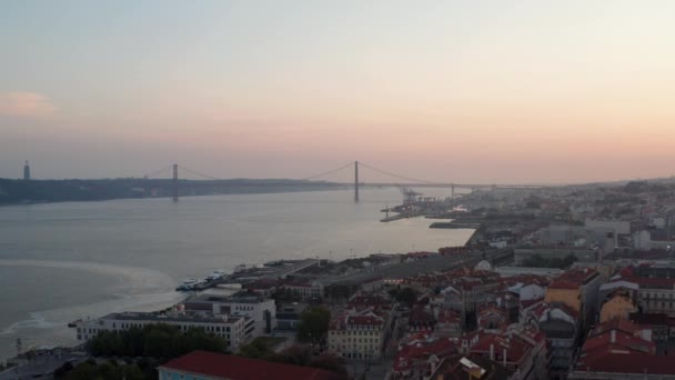 Aerial slider view of Ponte 25 de Abril red bridge across the sea canal in Lisbon, Portugal with houses in old city center — Video