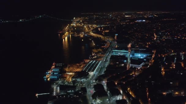 Aerial night view of urban city center of Lisbon with bright lights on houses, Ponte 25 de Abril bridge and coastal traffic by the sea — Stockvideo