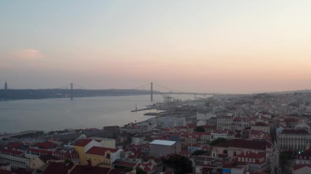 Slider aerial view of Ponte 25 de Abril red bridge in Lisbon, Portugal with rooftops of houses in the city center in the front — Video