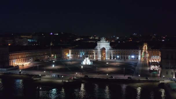 Вращающийся ночной вид с воздуха на площадь Фака-ду-Комери и памятник Арко да Руа Августа с зажженными огнями на берегу моря в центре города Лисбон — стоковое видео
