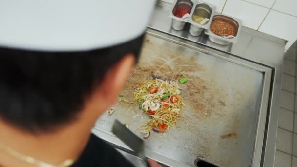 Sur la vue d'épaule de cuisinier professionnel mélangeant nouilles aux légumes sur une plaque chauffante dans la cuisine du restaurant. Plat de nouilles asiatiques traditionnelles — Video
