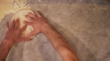 Masada pizza hamuru yapan profesyonel pizza şefinin genel manzarası. Ellerinin arasında pizza hamuru yuvarlayan bir aşçının tepeden aşağı görüntüsü