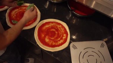 Profesyonel aşçı pizza hamuruna fesleğen yaprağı ekliyor. Restorandaki domates sosuyla kaplı.