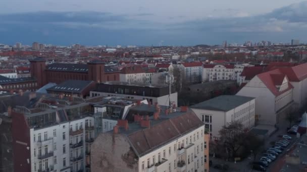 Roof top view of building in streets of Berlin near TV Tower, Fernsehturm after sunset. Panning footage of large city from drone flying low above houses. — Stock Video