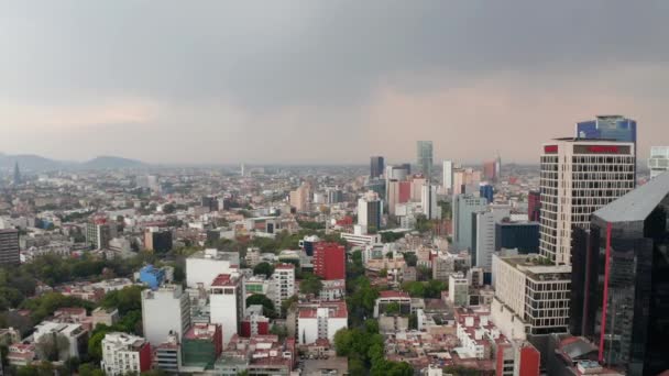 Şehrin üzerinde geriye doğru uçan drone kamera. Yüksek ofis binaları olan alçak konutlar. Yağmurdan önce şehir manzarası. Mexico City, Meksika. — Stok video