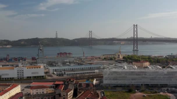 Vue aérienne descendante des bâtiments et du port sur la côte de Lisbonne avec le pont Ponte 25 de Abril et la statue du Sanctuaire du Christ Roi en arrière-plan — Video