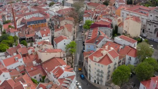 Aerial overhead top down view of yellow tram driving on the tracks through narrow residential streets between colorful houses in Lisbon urban city center — Stock Video