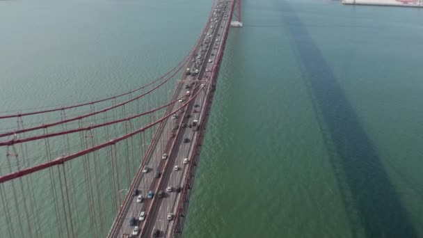 Inclinaison aérienne révélant un trafic automobile achalandé sur plusieurs voies traversant le pont rouge Ponte 25 de Abril vers le centre-ville urbain de Lisbonne, Portugal — Video