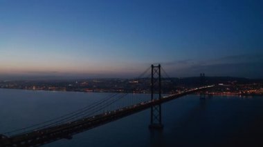 Lizbon ve Almada 'yı bağlayan 25 Nisan Köprüsü' nün gece hava görüntüsü. Tegus nehri üzerinde, kablo destekli karayolu köprüsündeki araba farları. İHA ileri uçuyor. Lizbon, Portekiz 'in başkenti.