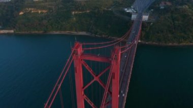 İHA köprü sütununun üzerinde uçuyor ve kamera aşağı eğiliyor. Nehrin üzerinde kırmızı, çok şeritli bir köprü. Lizbon, Portekiz 'in başkenti.