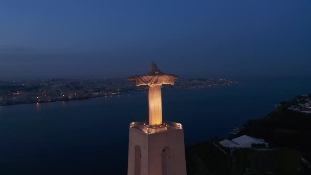 Gece dronu uzanmış elleriyle büyük aydınlatılmış İsa heykeline doğru uçuyor. Gün batımından sonra Almada 'daki Kral Mabet' in havadan görünüşü. Lizbon, Portekiz 'in başkenti. — Stok video