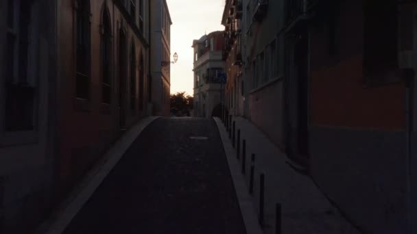 ドローンカメラは夕方の日没の空に対して暗い狭い通りを飛んでいます。ポルトガルの首都リスボン. — ストック動画