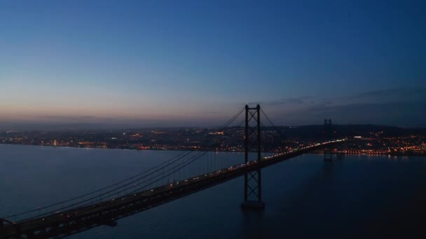 Vista aérea noturna da Ponte 25 de Abril que liga Lisboa e Almada. Faróis de carro na ponte rodoviária sobre o rio Tegus. Um drone a voar para a frente. Lisboa, capital de Portugal. — Vídeo de Stock