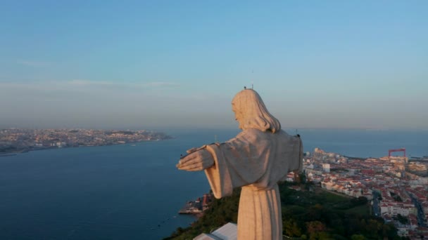 Große steinerne Jesus-Statue, erleuchtet von den letzten Sonnenstrahlen des Tages. Drohnen-Kamera fliegt hinter dem Christus-König-Heiligtum in Almada. Lissabon, Hauptstadt von Portugal. — Stockvideo
