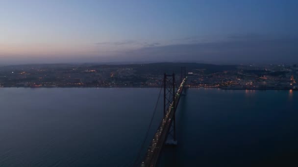 Night aerial view of 25th of April Bridge connecting Lisbon and Almada. Many car headlights on cable-stayed highway bridge over Tegus river. Drone flying forwards. Lisbon, capital of Portugal. — Stock Video