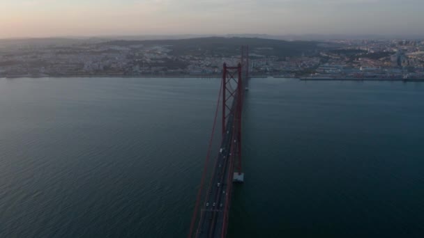 Evening aerial view of 25th of April Bridge connecting Lisbon and Almada. Long cable-stayed highway bridge over Tegus river. Drone rotating around. Lisbon, capital of Portugal. — Stock Video
