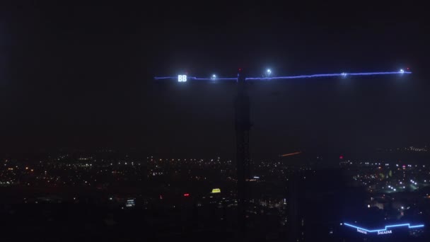 Arm av konstruktion kran belyst med blå neon ljus och två stora bokstäver B. Nattstadsbild med ljus i bakgrunden. Flygfoto från drönare. Dallas, Texas, USA — Stockvideo